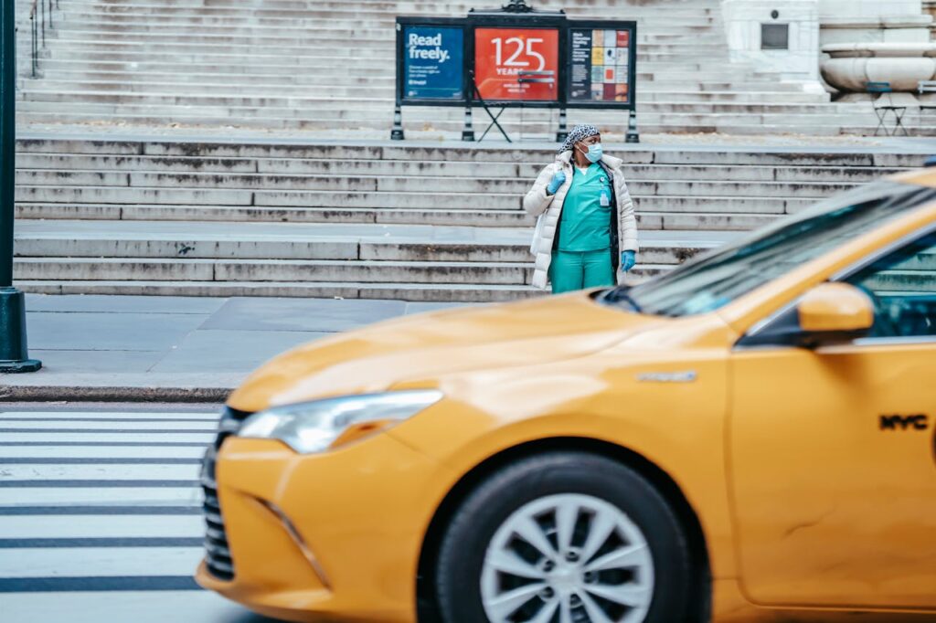 pexels-photo-6097736 African American female doctor in uniform looking away from sidewalk against taxi cab on roadway in town